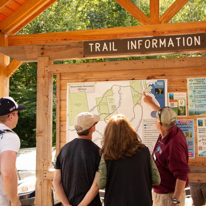 A man in a red sweatshirt points out points on a map to a small group of people