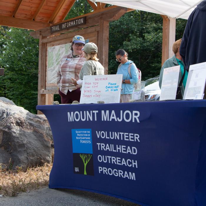 A blue table cloth reads "Mt Major Volunteer Trailhead Outreach Program"