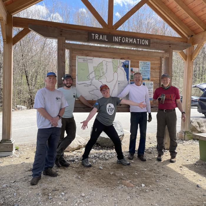 A group of smiling people pose in front of a trail kiosk