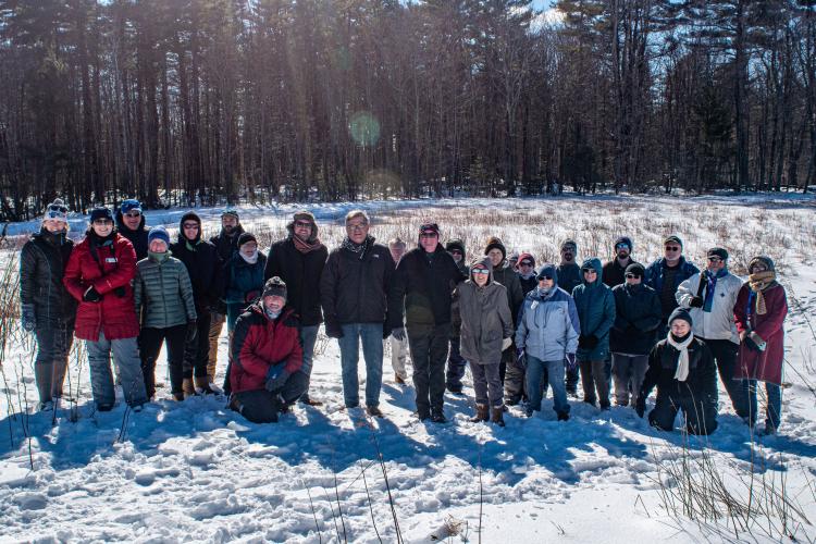 A group gathers in front of a snowy forest for a photo commemorating the expansion of Champlin Forest.