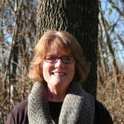 Rita Carroll poses against the trunk of a tree.