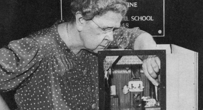 Frances Glessner Lee is shown in black and white as she uses tweezers on her diorama.