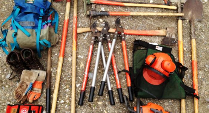 Forestry tools including gloves and a timber jack are organized on the ground.