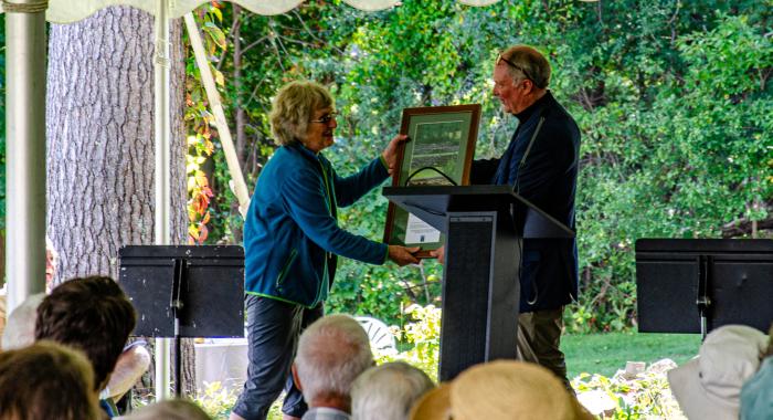 Volunteer of the Year Janet Hill accepts a plaque on stage from President Jack Savage.