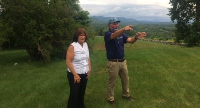 Congresswoman Kuster and SPNHF President Jack Savage standing in front of misty view of the White Mountains at The Rocks in Bethlehem.