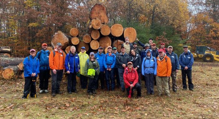 Volunteer land stewards and staff pose in front of logs at the Wilkins Campbell log landing
