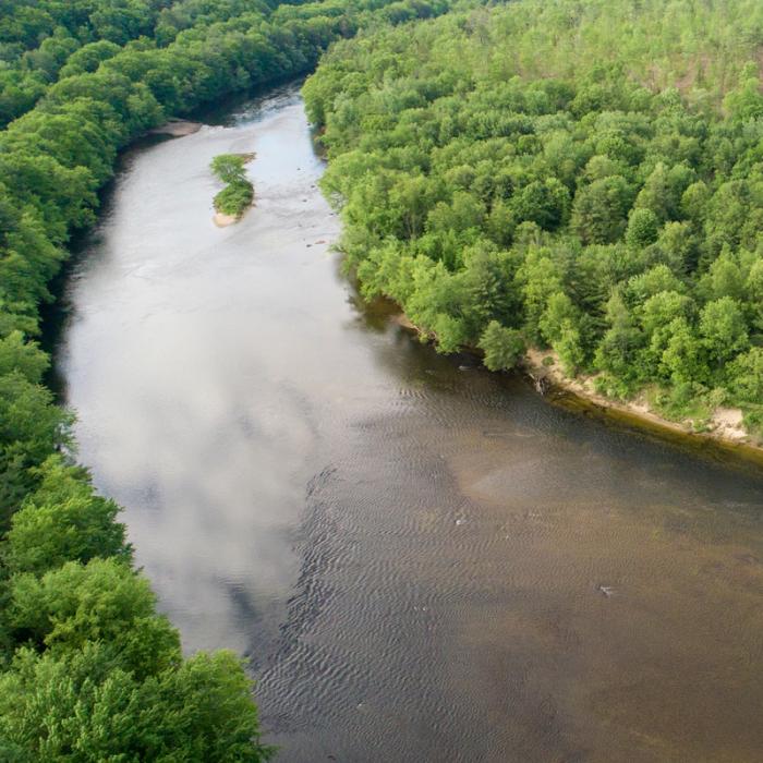 A view from above of a bend in the Merrimack River, lined with green forests.