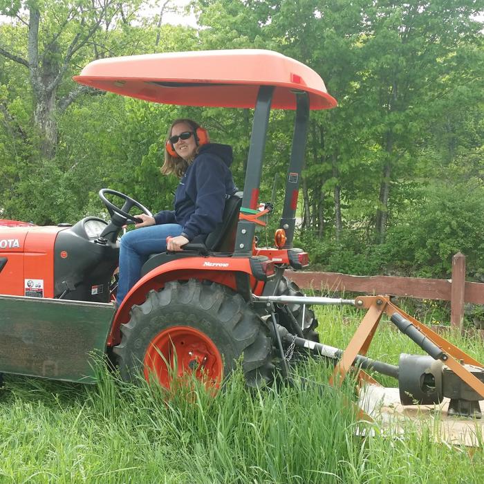 A woman on a tractor mows a field.