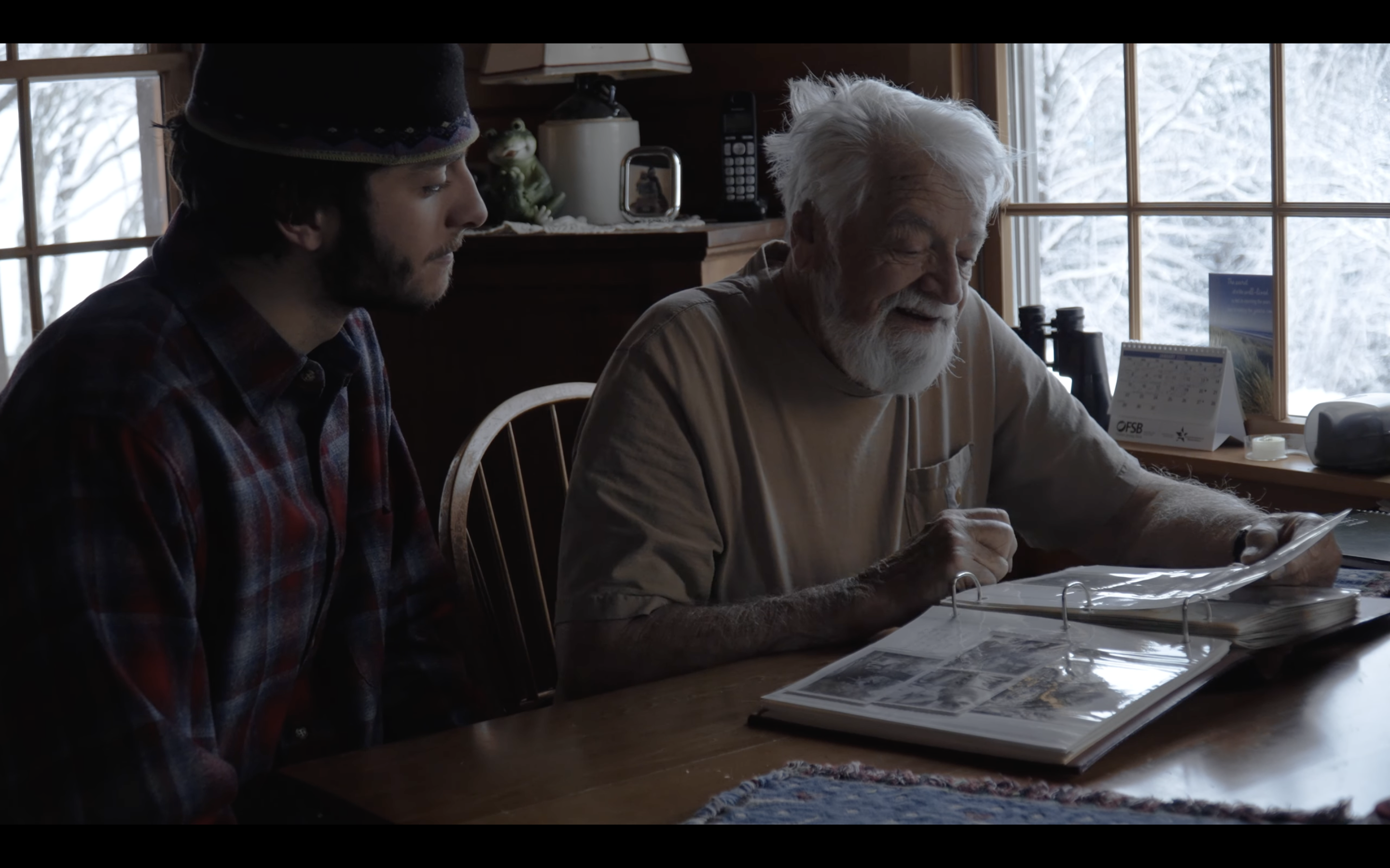 Older man and grandson look at a book at a table. 