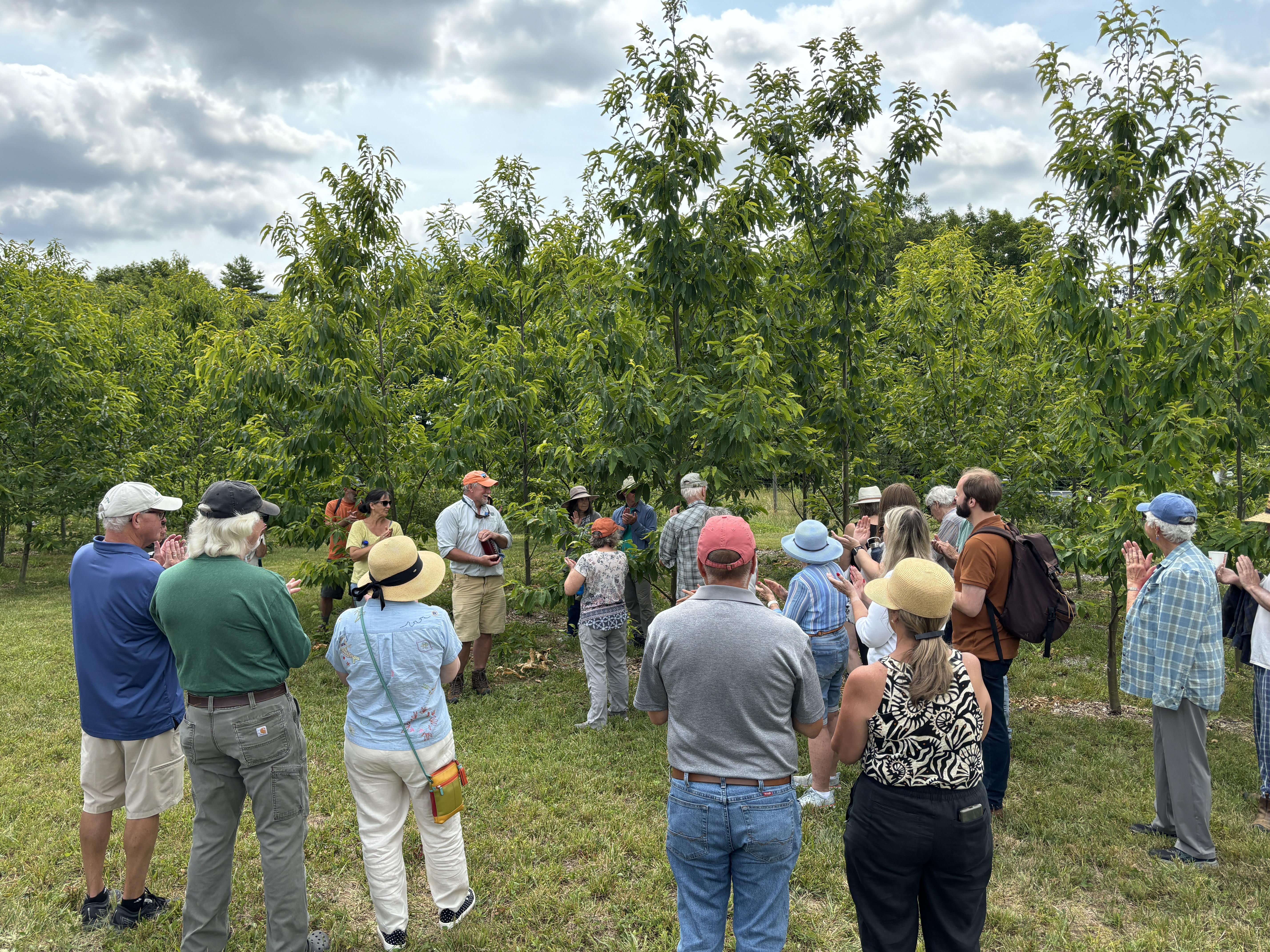 A crowd listens in front of the orchard.