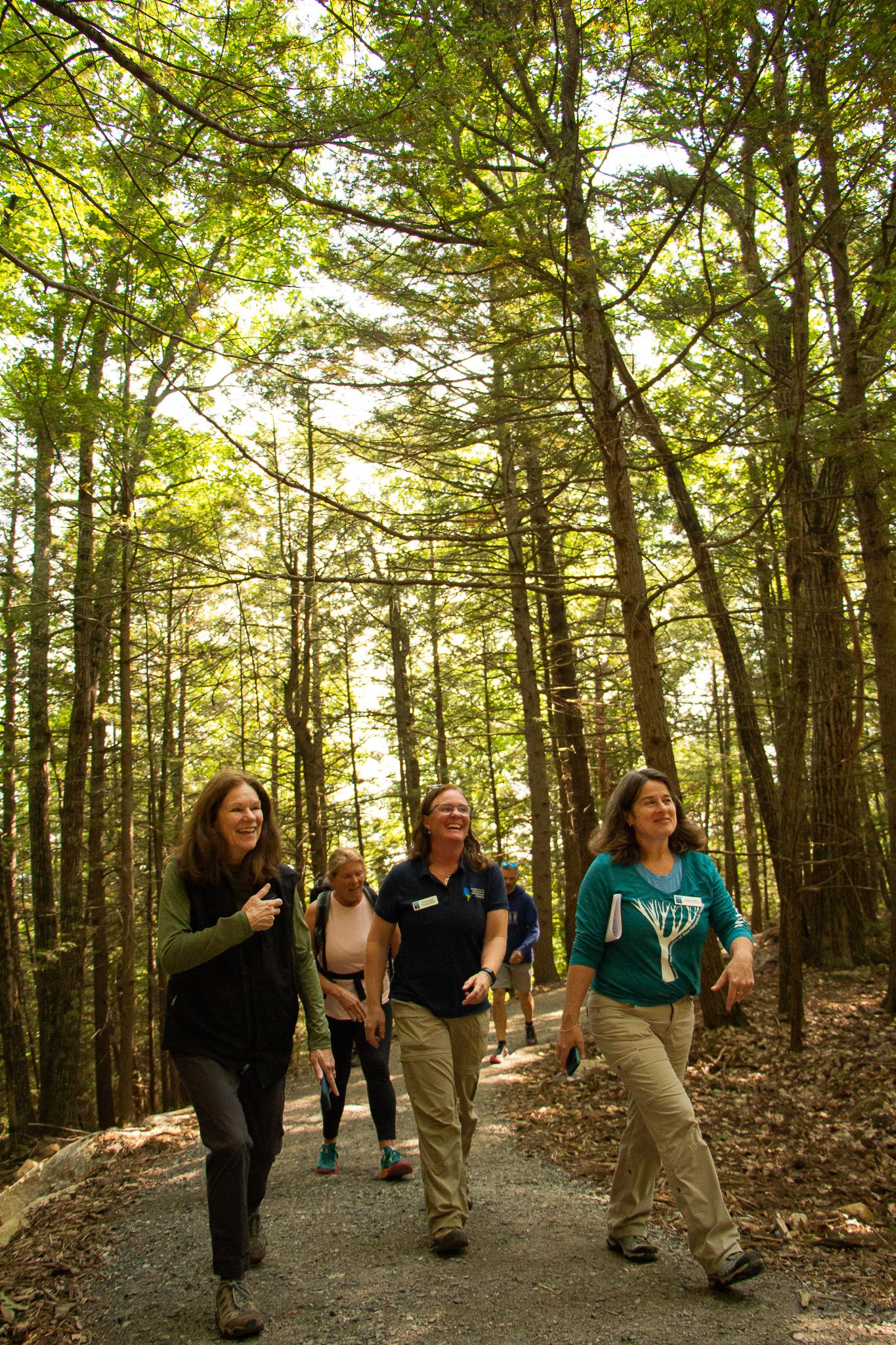 Three women walk on a gravel path in the woods. 