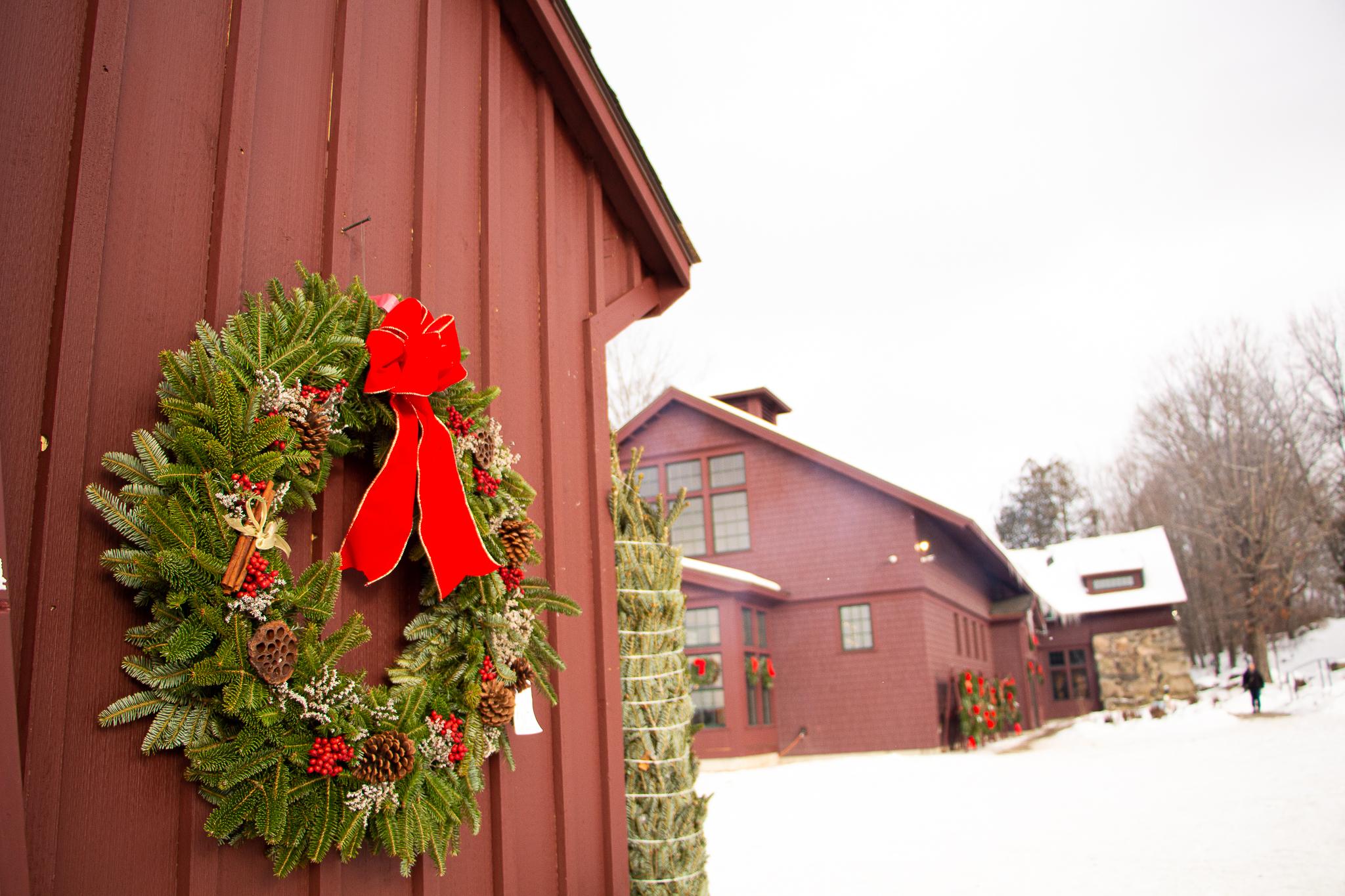 A large evergreen wreath with a red bow on the side of a wooden shed. 