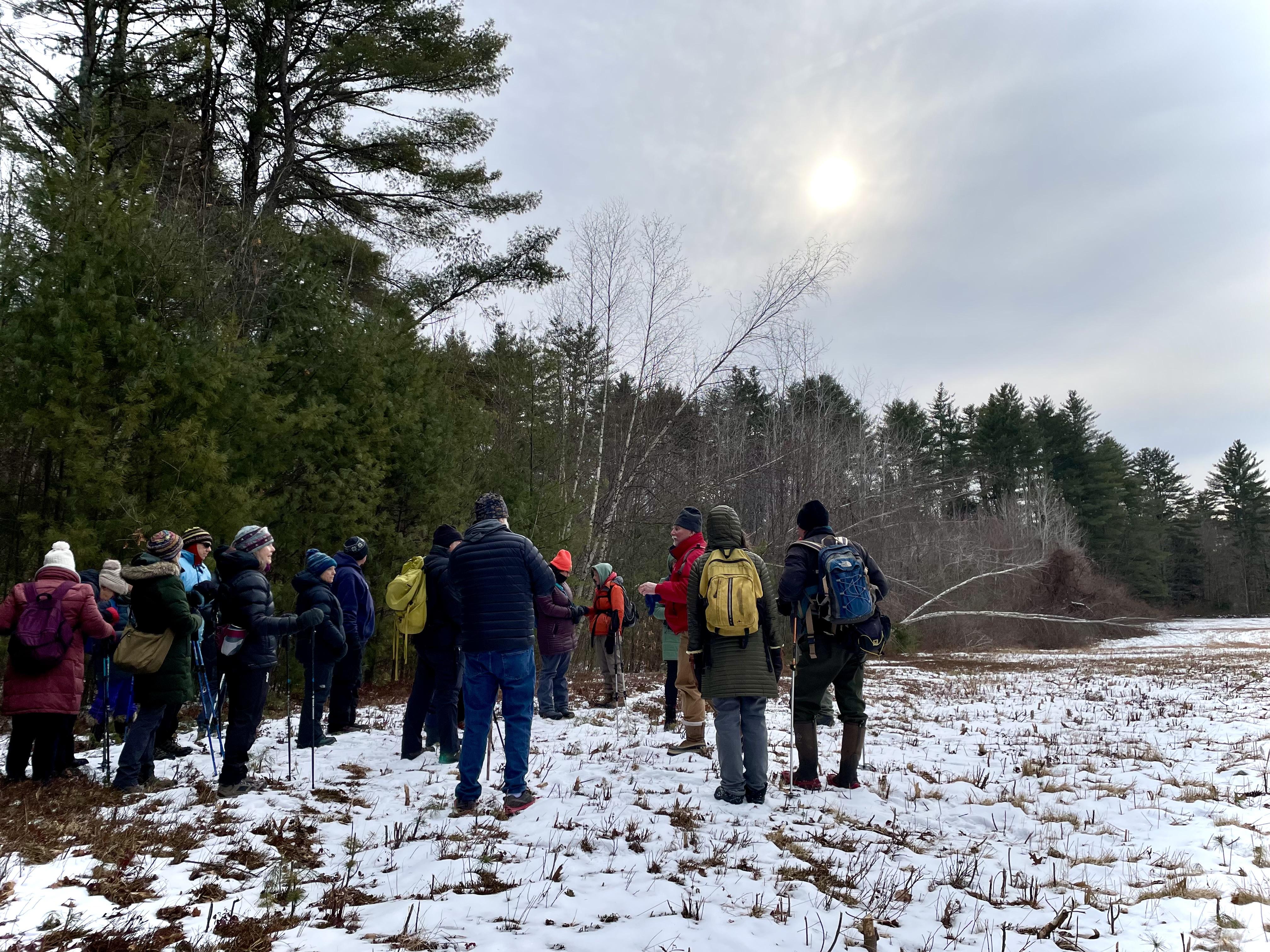 A group of hikers listen to a guide speaking in a snowy field. 