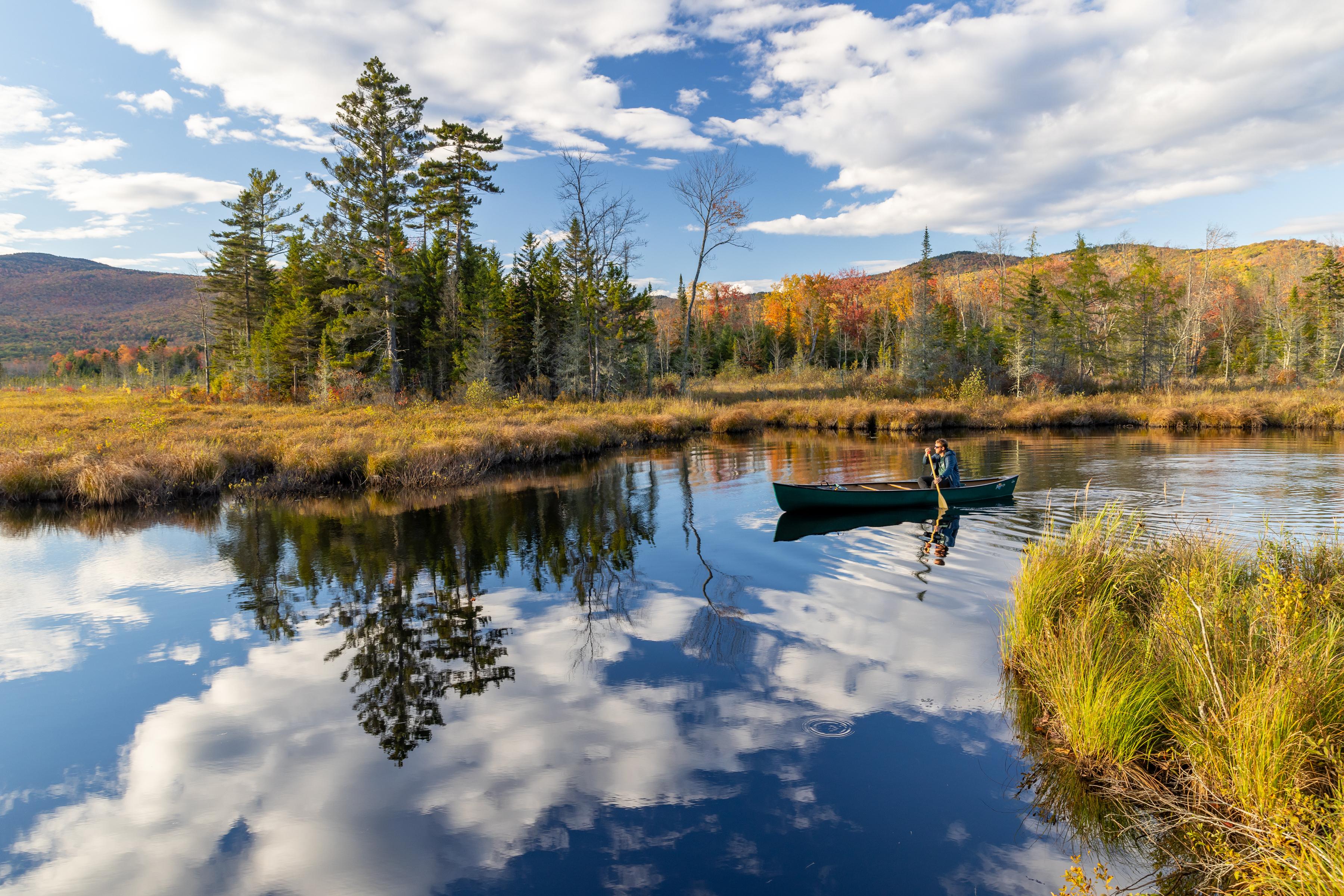 A kayaker glides over a lake on a sunny fall day.