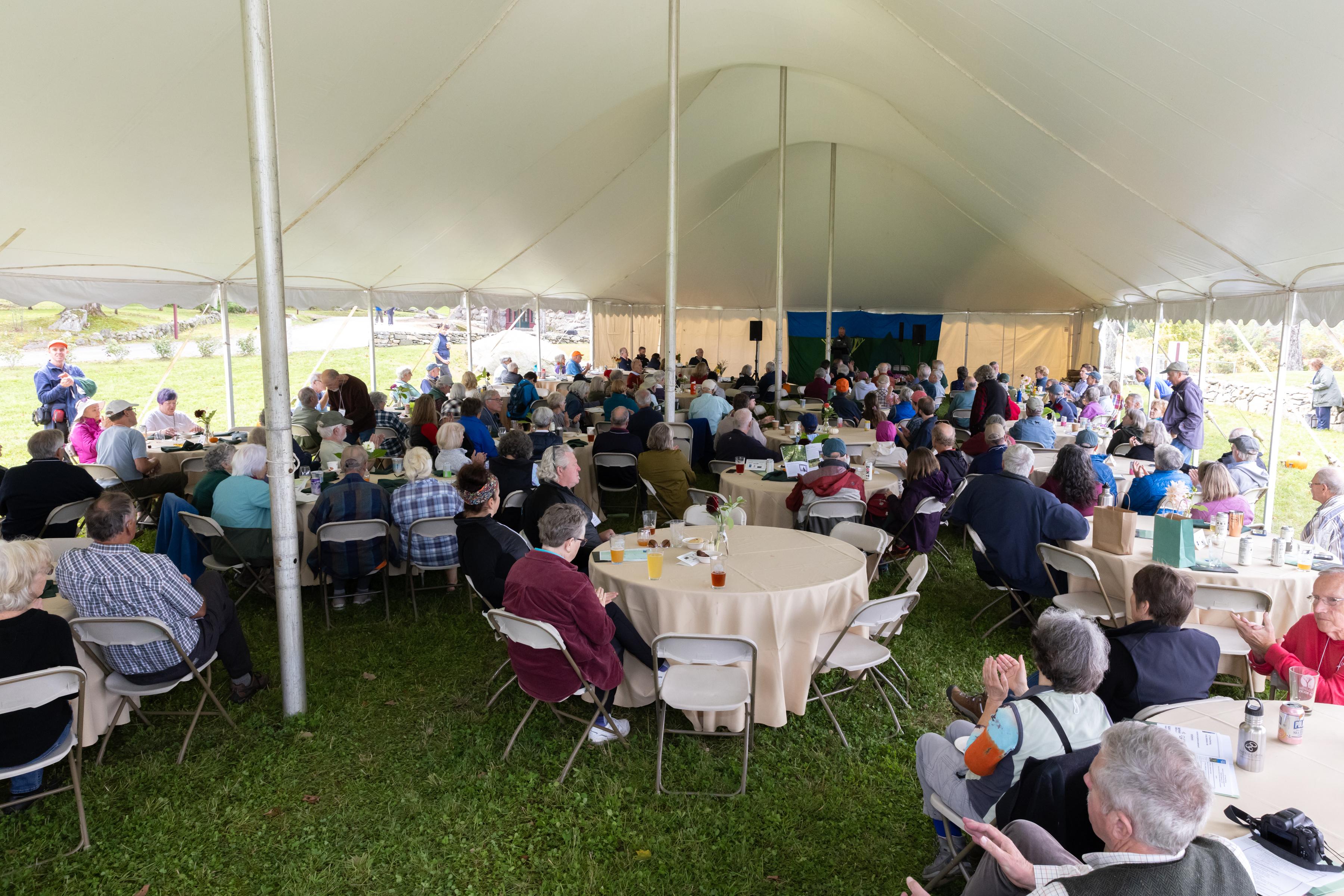 Attendees watch the meeting from under the tent.