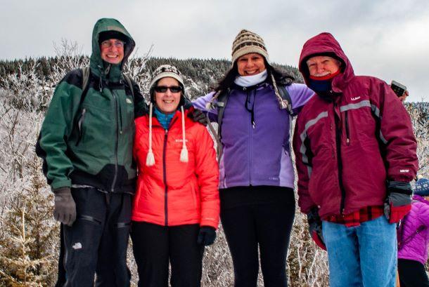 A group of four hikers stands at the top of a snowy viewpoint on Mount Monadnock.