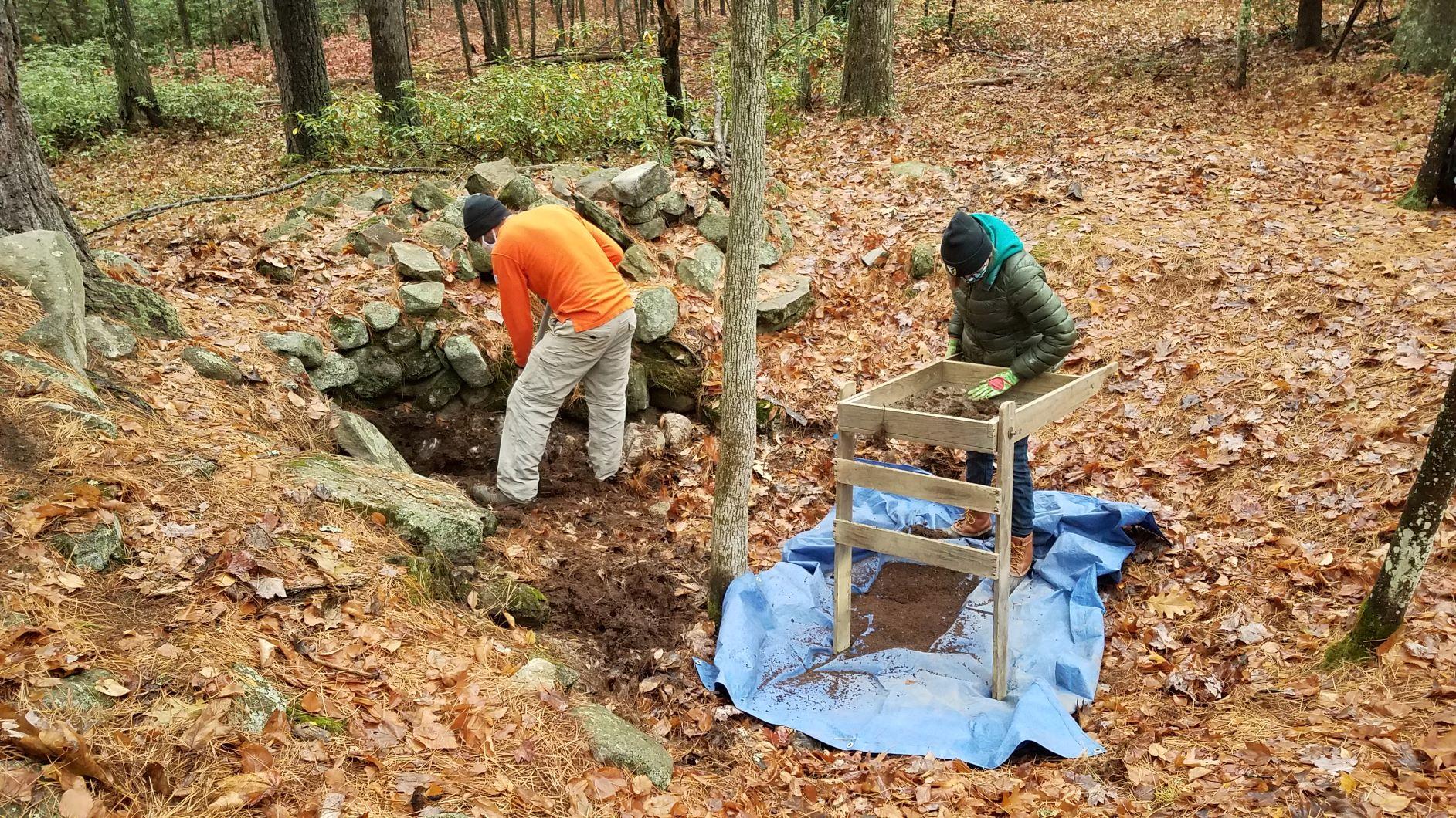 Two archaeologists look down into a cellar hole at Monson Center.