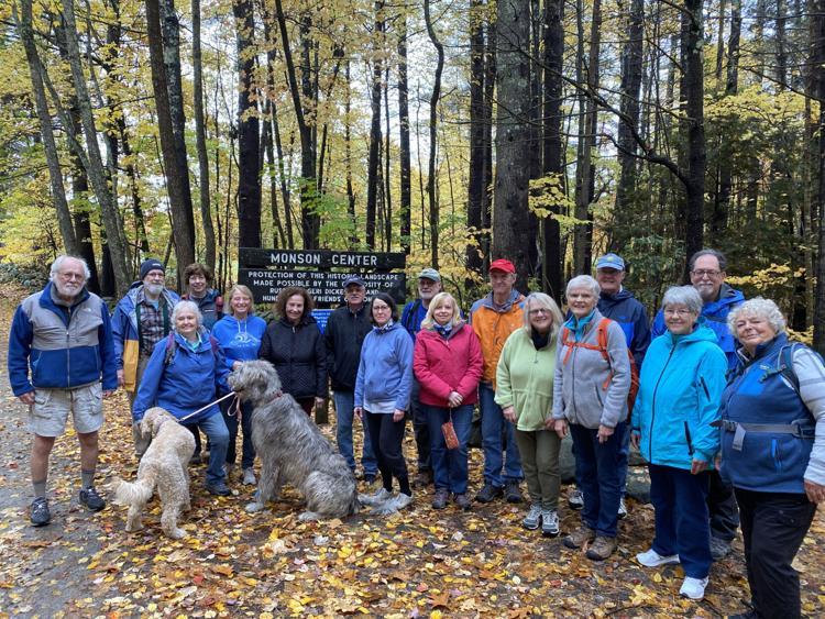 Colorfully clad group of older hikers pose at Monson Center sign