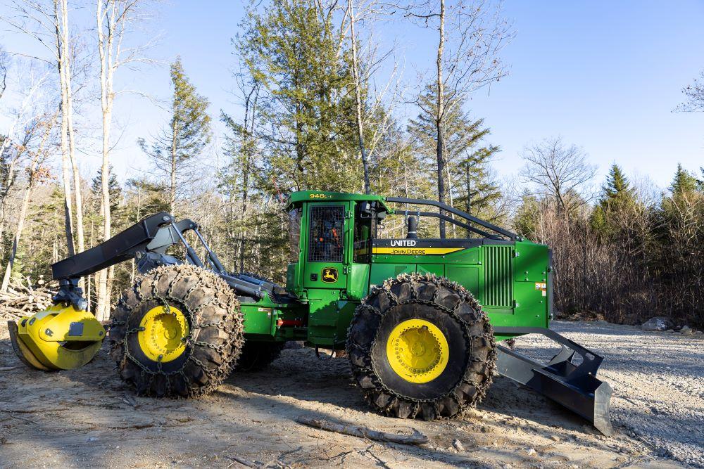 A green grapple skidder parked on log landing at active winter timber  harvest