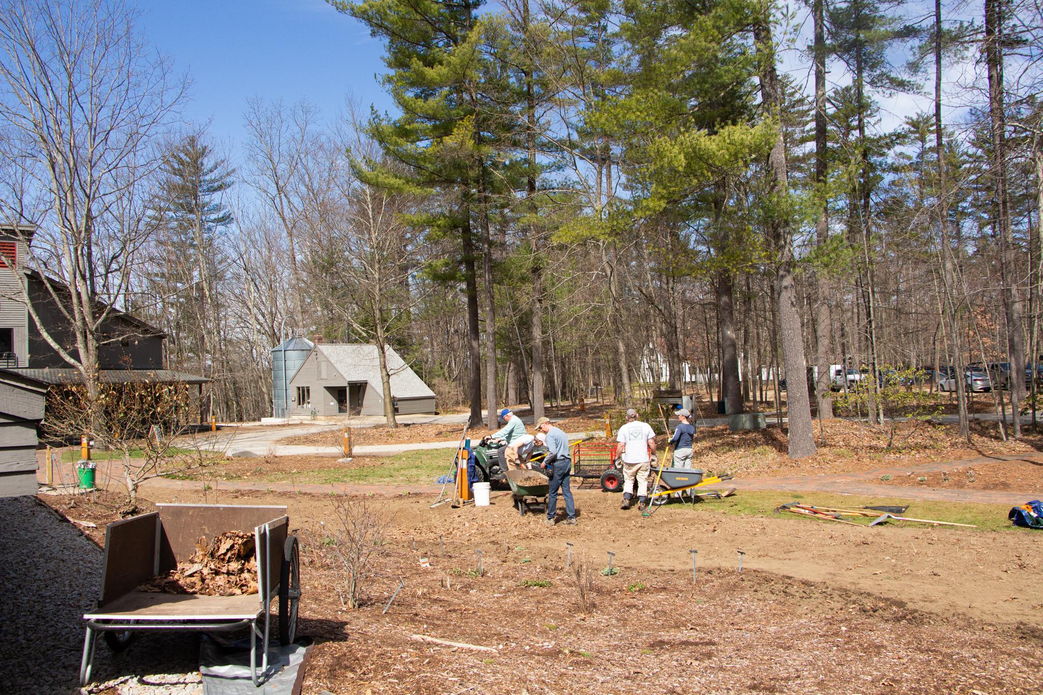 A group of workers stand down the hill from the camera, crowded around a wheel barrow