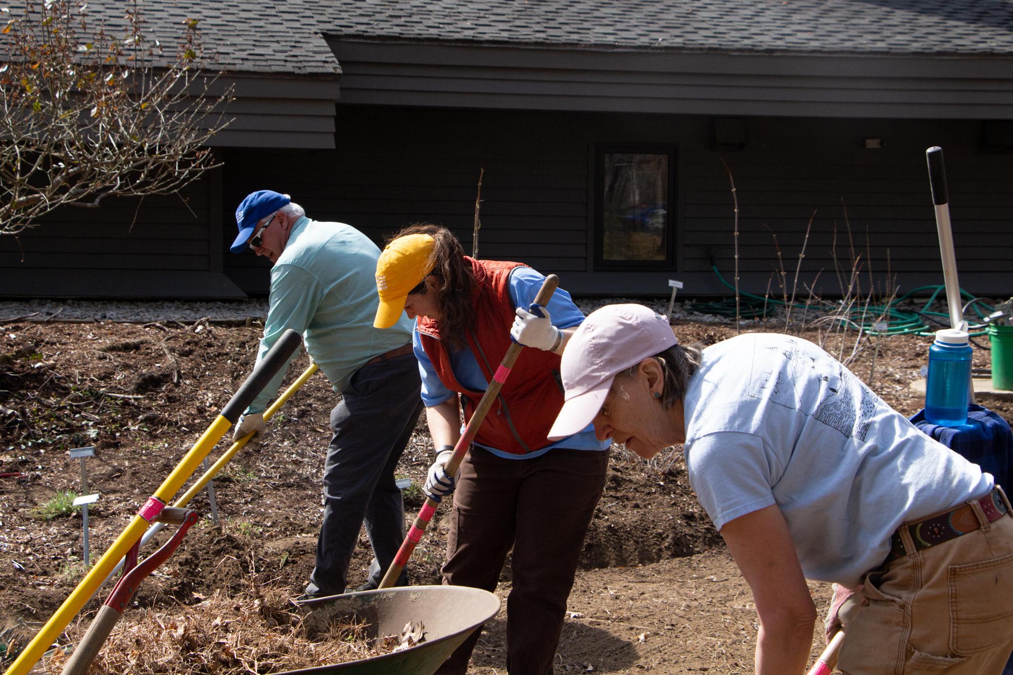 Three people rake leaves side by side. 