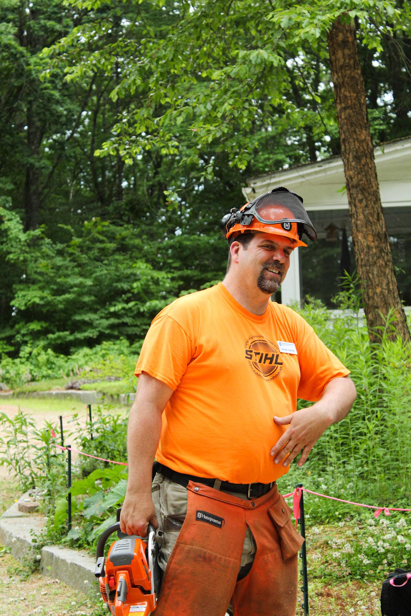 Man in orange shirt and hardhat holding chainsaw and smiling