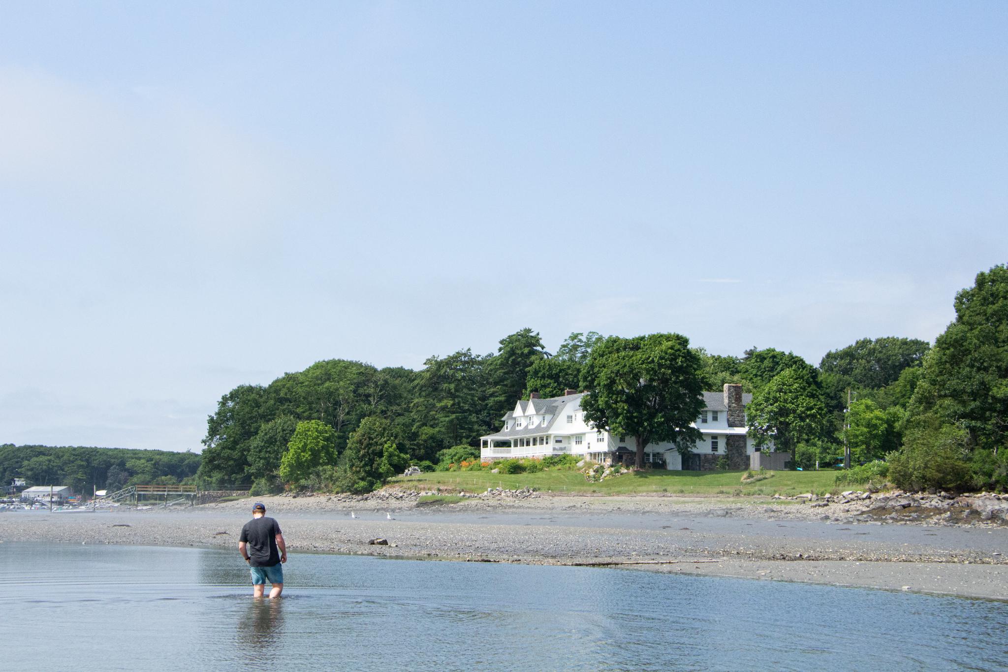 A young man walks through shallow water towards the shore. 