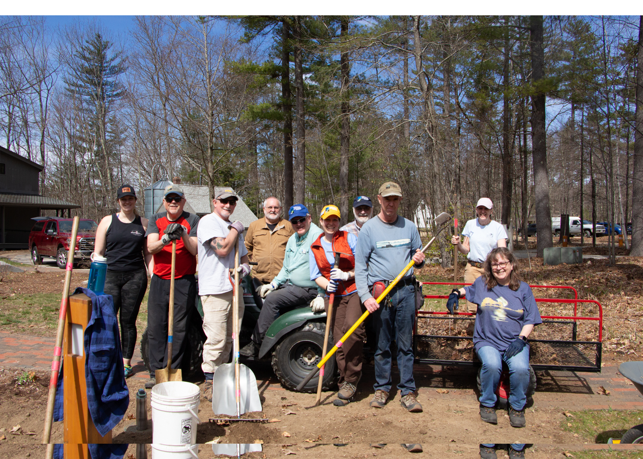 a group of people holding yard tools pose around a 4 wheeler 