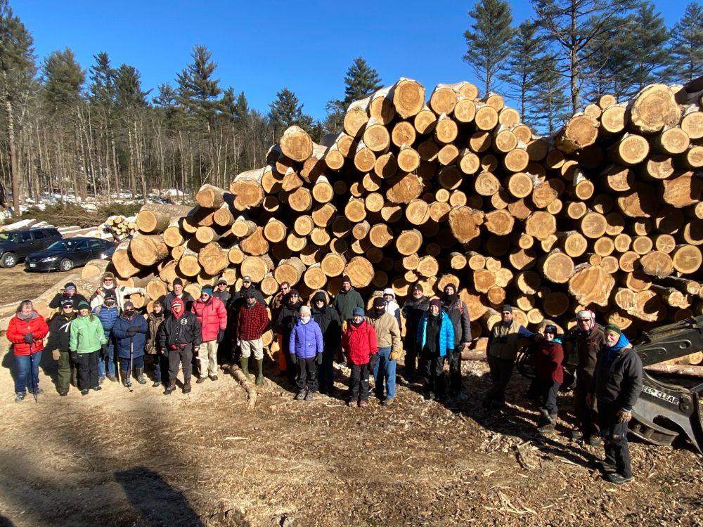 Huge log pile on landing in background with people in colorful winter parkas in foreground on timber landing in Lempster on Jan 22, 2022 