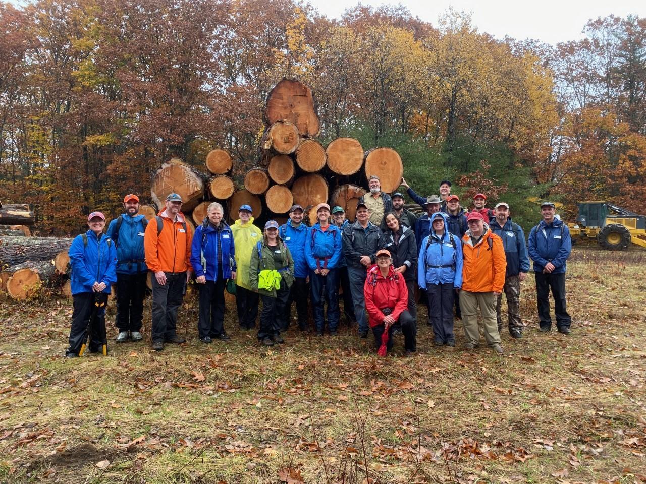 Volunteer land stewards and staff pose in front of logs at the Wilkins Campbell log landing