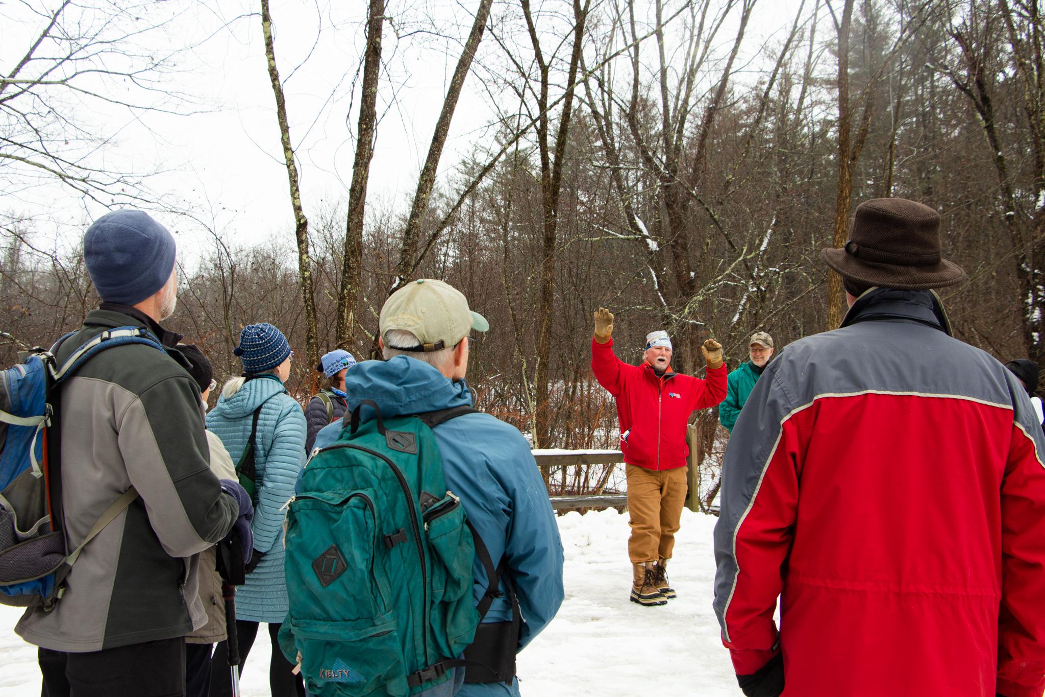 A man speaks to a crowd who is photographed from behind 