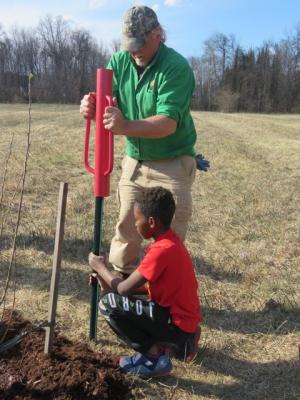 Dave Anderson and a student use a tool to dig a hole for a tree.