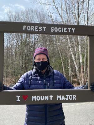 A volunteer holds a frame up that says "I love Mount Major" on Earth Day.
