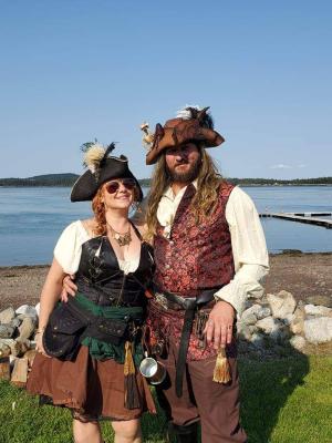 Two people dressed as pirates stand in front of the ocean 