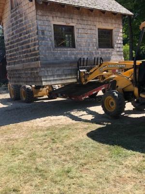 A small wood shed is lifted by a front-end loader.