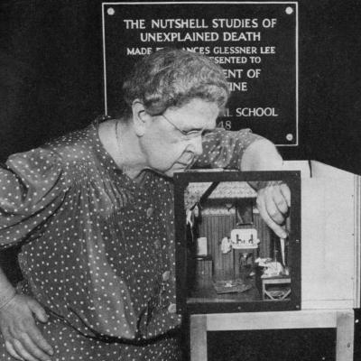 Frances Glessner Lee is shown in black and white as she uses tweezers on her diorama.