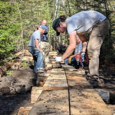 A man wearing a tshirt and gloves works on a small bridge using a hammer. 