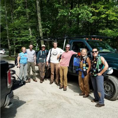 Group of trail crew volunteers leaning on a pickup truck in a dirt parking lot