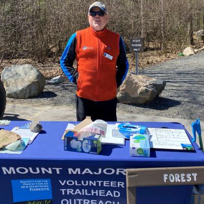 A volunteer stands at the VTOP table at the trailhead of Mt. Major.