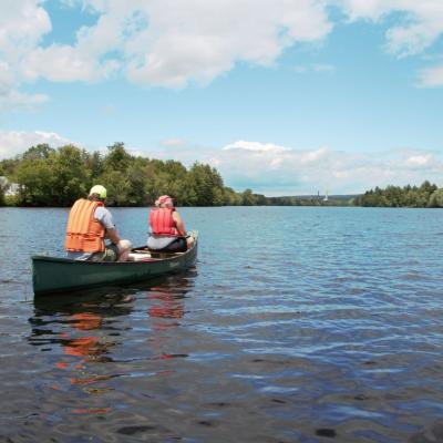 Two people in lifejackets in a canoe on the Merrimack River as seen from behind.