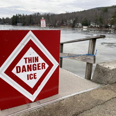 A red sign reading "Danger Thin Ice" is hung on a boat dock near a frozen lake