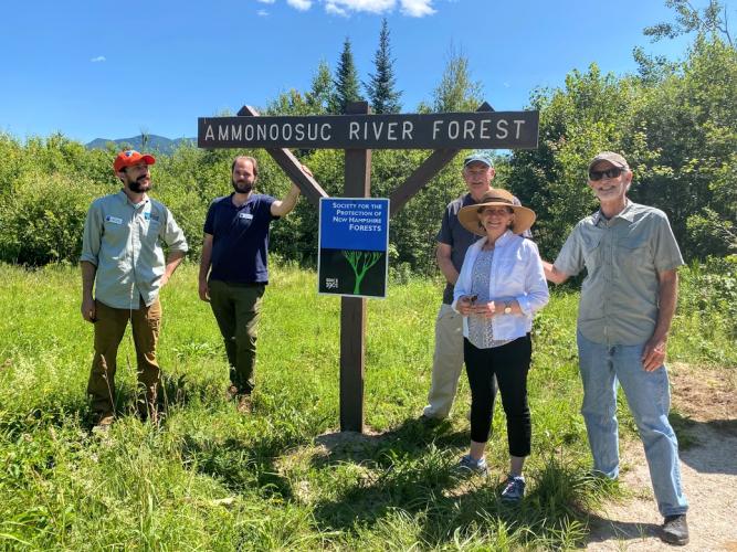 A group of staff and community members pose at the entrance to the Ammonoosuc River Forest.