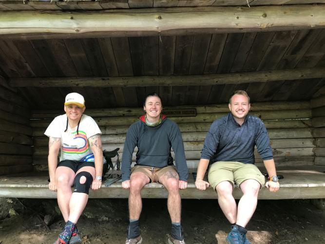 A group of three hikers sits on a bench at the General Washington Shelter on the Monadnock-Sunapee Greenway.