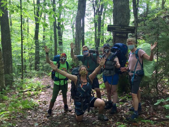 A group of masked hikers poses in front of a sign on the Monadnock-Sunapee Greenway trail.