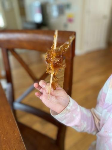 A hand holds maple taffy wound on a popsicle stick.