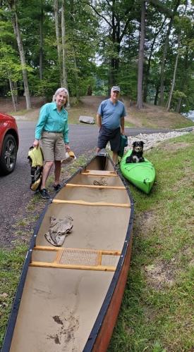 Two people stand near kayaks with a dog in the back vessel.