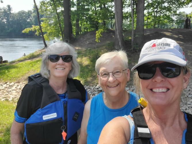 A group of female kayakers in life jackets pose for a selfie on the river.