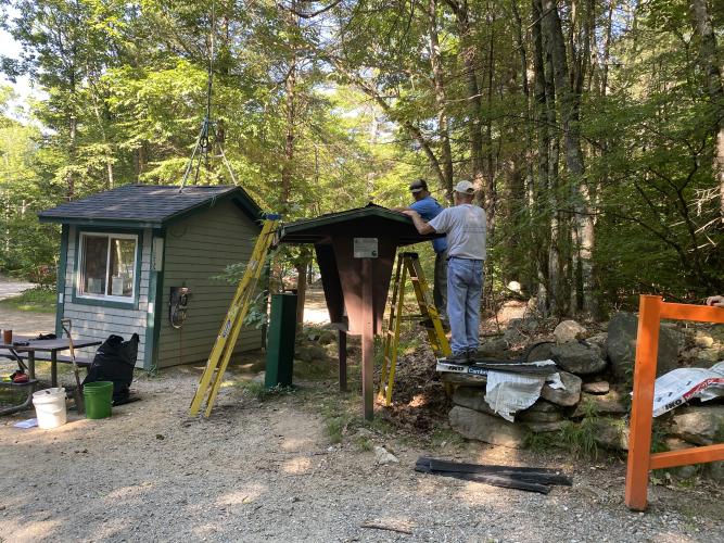 A volunteer helps put a new roof on a trailhead kiosk.