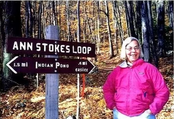 Ann Stokes poses beside a sign for the trail named after her.