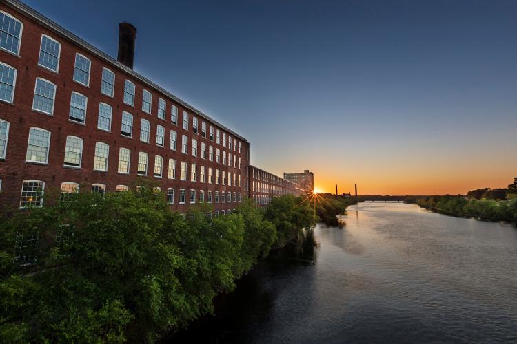 A river at sunset winds past a former mill building in Lowell.